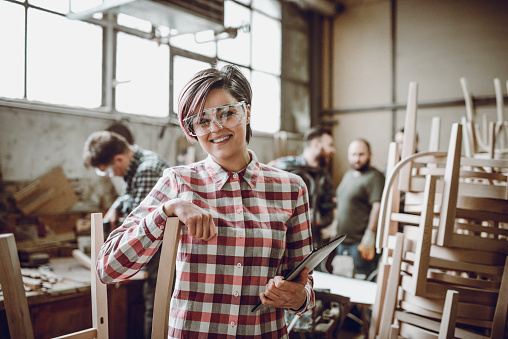Young Smiling Carpenter in Front of Working Team in her Work Shop
